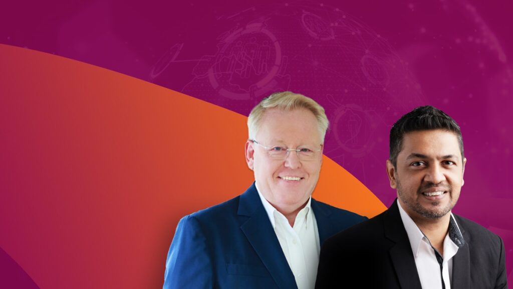 Two men in formal wear stand against a background with red and purple hues, featuring abstract digital graphics reminiscent of an industrial network. One man has light hair and wears a blue jacket, while the other has dark hair and sports a black jacket.