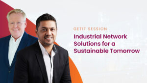 Two men smiling, one of south asian descent, at a "getit session" titled "industrial network solutions for a sustainable tomorrow," with an industrial backdrop.