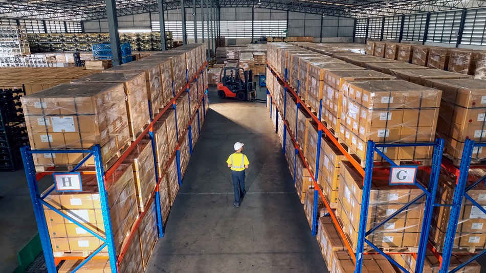 A warehouse worker in a yellow safety vest walks between tall shelves stacked with boxes, while an ethical forklift operator ensures safe and responsible handling in the background.