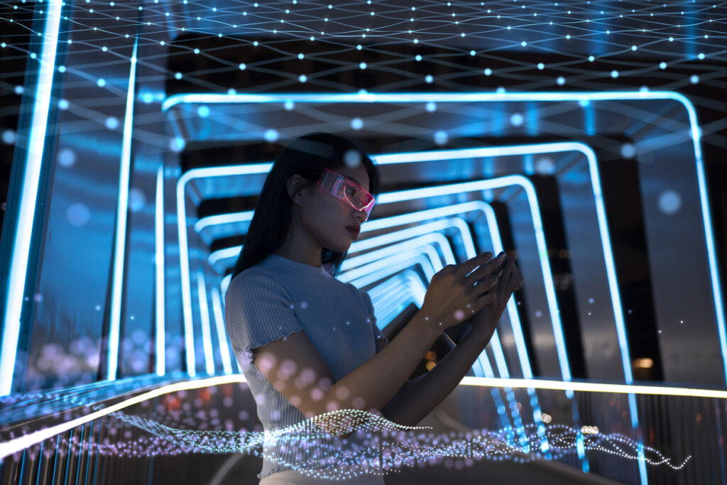 A person wearing futuristic glasses interacts with a handheld device in a neon-lit, technologically advanced environment.
