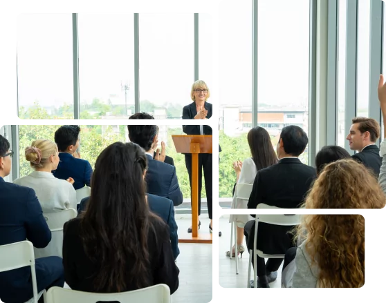 A woman stands at a podium addressing an audience seated on white chairs in a bright room with large windows. Audience members, eager to getit, raise their hands.