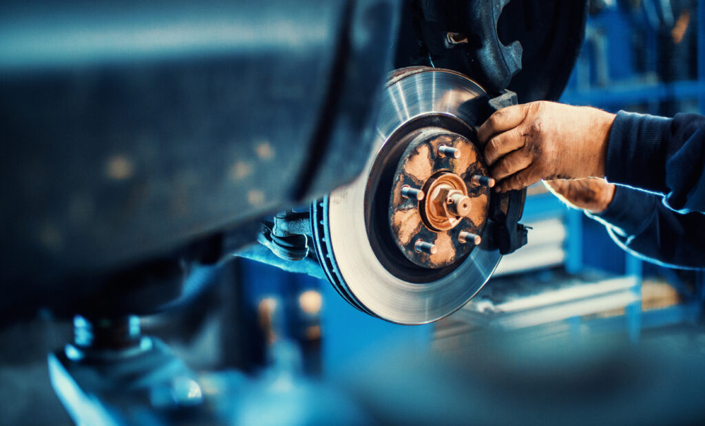 Mechanic's hands working on a car brake system, focusing on the Akebono brake rotor and caliper in a workshop setting.