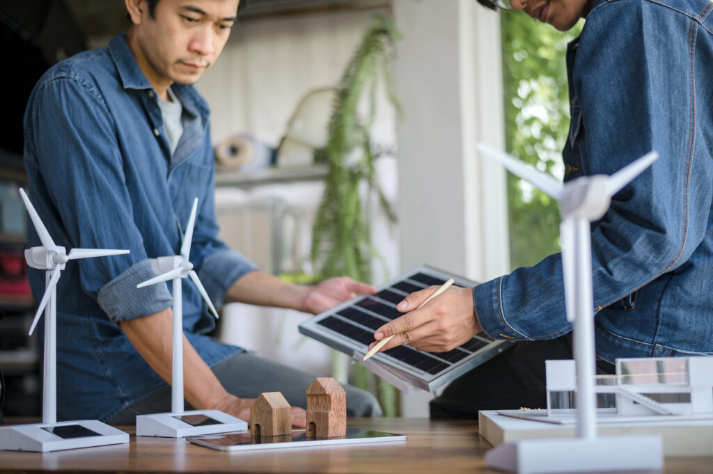 Two people examine solar panels and wind turbine models on a table.