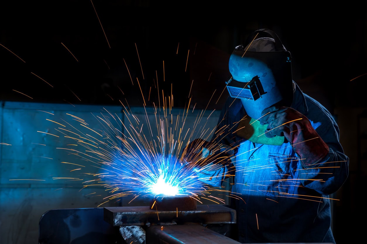 A welder in protective gear skillfully melds metal with sparks flying.