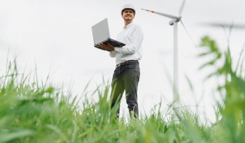Engineering man using laptop to checking wind turbine generator of electricity at outdoor, blue sky and cloudy background